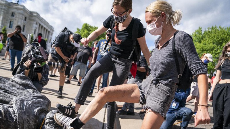 Activists bring down the Christopher Columbus statue in front of the Capitol, Wednesday, June 10, 2020, in St. Paul, Minn. A rope was thrown around the 10-foot bronze statue and it was pulled off its stone pedestal. The protesters included Dakota and Ojibwe Indians who consider Columbus as a symbol of genocide against Native Americans. State Patrol troopers in helmets stood by at a distance but did not try to stop the protesters. (Leila Navidi/Star Tribune via AP)