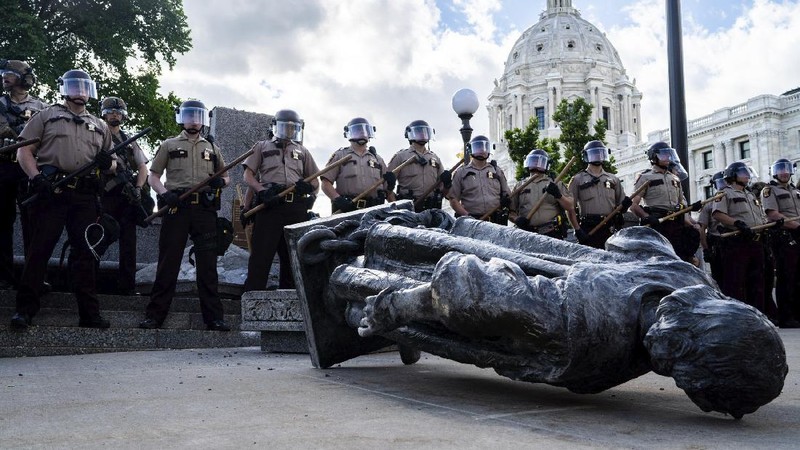 Activists bring down the Christopher Columbus statue in front of the Capitol, Wednesday, June 10, 2020, in St. Paul, Minn. A rope was thrown around the 10-foot bronze statue and it was pulled off its stone pedestal. The protesters included Dakota and Ojibwe Indians who consider Columbus as a symbol of genocide against Native Americans. State Patrol troopers in helmets stood by at a distance but did not try to stop the protesters. (Leila Navidi/Star Tribune via AP)