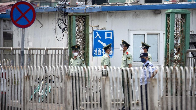 A  police officer watches as workers spray a sidewalk near the Xinfadi wholesale food market district in Beijing, Saturday, June 13, 2020. Beijing closed the city's largest wholesale food market Saturday after the discovery of seven cases of the new coronavirus in the previous two days. (AP Photo/Mark Schiefelbein)
