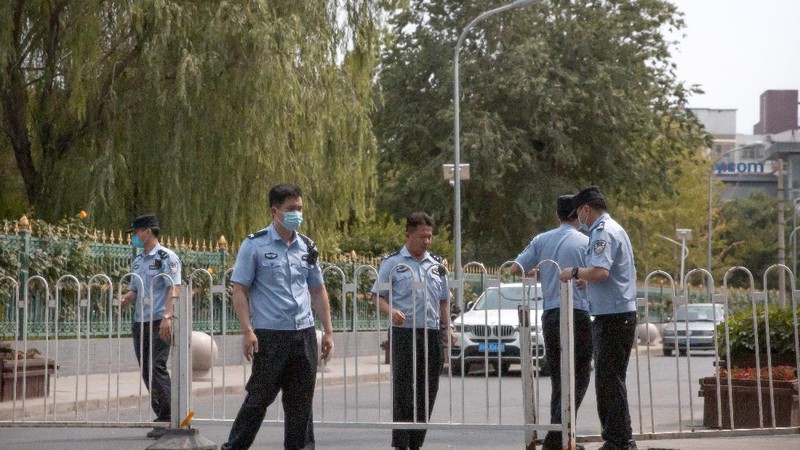 A  police officer watches as workers spray a sidewalk near the Xinfadi wholesale food market district in Beijing, Saturday, June 13, 2020. Beijing closed the city's largest wholesale food market Saturday after the discovery of seven cases of the new coronavirus in the previous two days. (AP Photo/Mark Schiefelbein)