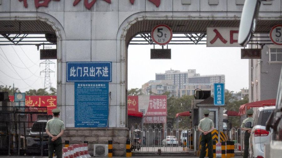 A  police officer watches as workers spray a sidewalk near the Xinfadi wholesale food market district in Beijing, Saturday, June 13, 2020. Beijing closed the city's largest wholesale food market Saturday after the discovery of seven cases of the new coronavirus in the previous two days. (AP Photo/Mark Schiefelbein)