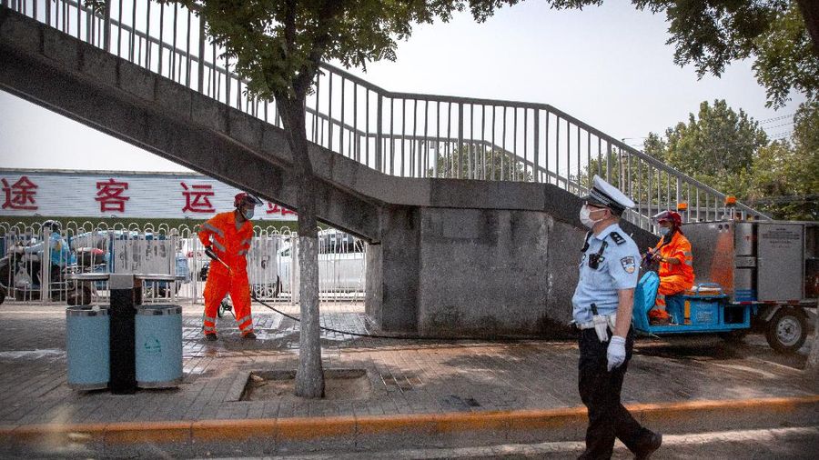 A  police officer watches as workers spray a sidewalk near the Xinfadi wholesale food market district in Beijing, Saturday, June 13, 2020. Beijing closed the city's largest wholesale food market Saturday after the discovery of seven cases of the new coronavirus in the previous two days. (AP Photo/Mark Schiefelbein)