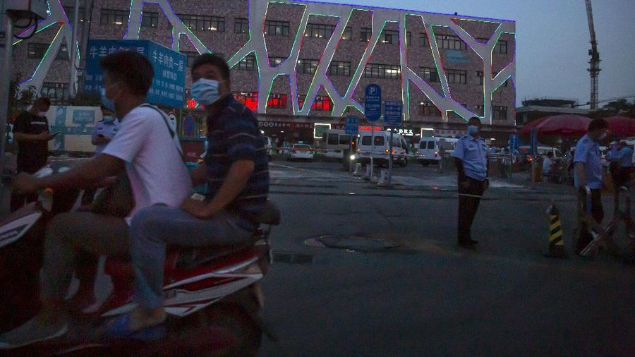 A  police officer watches as workers spray a sidewalk near the Xinfadi wholesale food market district in Beijing, Saturday, June 13, 2020. Beijing closed the city's largest wholesale food market Saturday after the discovery of seven cases of the new coronavirus in the previous two days. (AP Photo/Mark Schiefelbein)