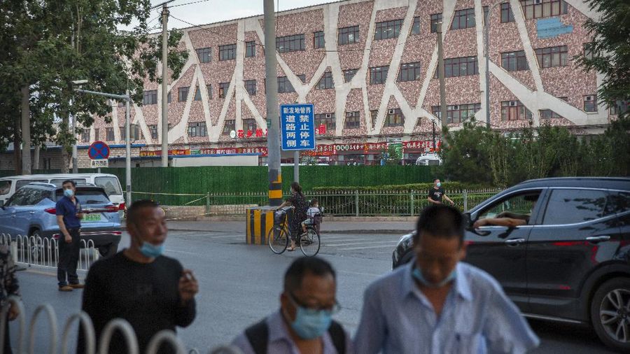People wearing face masks to protect against the new coronavirus walk past a building holding a beef and lamb market in Beijing that was closed by authorities after it was visited by a person who tested positive for COVID-19, Friday, June 12, 2020. Local authorities announced on Thursday a 52-year-old man had become the city's first confirmed case of local transmission in weeks after he arrived at a clinic complaining of fever. The official Xinhua News Agency said two other cases of COVID-19 were confirmed in Beijing on Friday. (AP Photo/Mark Schiefelbein)
