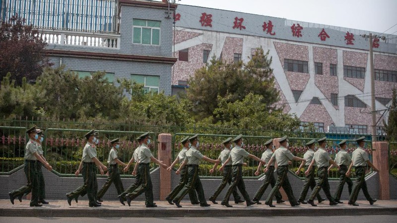 A  police officer watches as workers spray a sidewalk near the Xinfadi wholesale food market district in Beijing, Saturday, June 13, 2020. Beijing closed the city's largest wholesale food market Saturday after the discovery of seven cases of the new coronavirus in the previous two days. (AP Photo/Mark Schiefelbein)