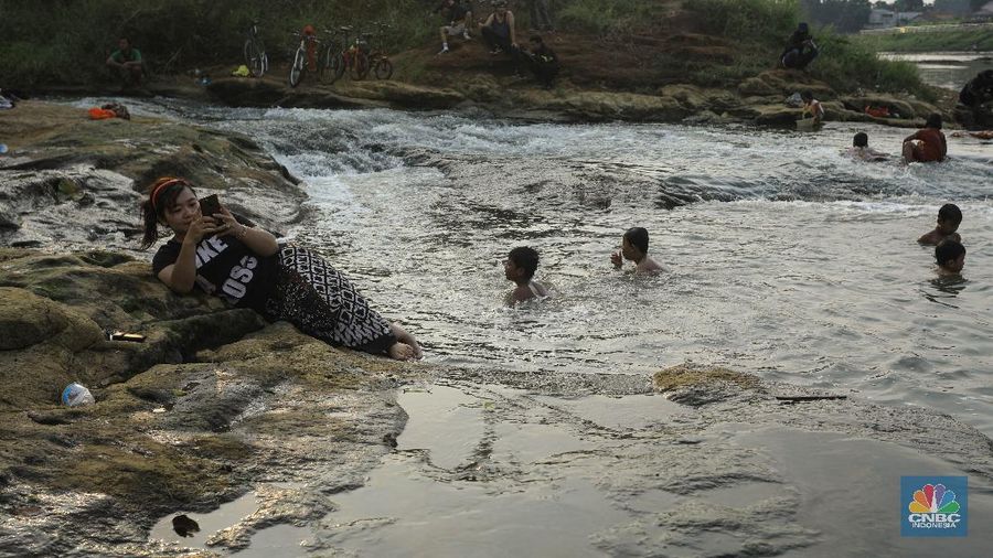 Warga berfoto dengan latar belakang aliran Kali Angke di Situ Lengkong Wetan, Serpong, Tangerang Selatan, Banten, Jumat 12 Juni 2020. Lokasi tersebut menjadi alternatif bagi warga untuk berwisata lokal di tengah masih berlangsungnya penerapan Pembatasan Sosial Berskala Besar (PSBB) di Tangerang Raya untuk menekan penyebaran coronavirus (Covid-19)  (CNBC Indonesia/ Andrean Kristianto)