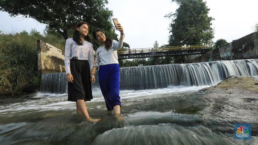 Warga berfoto dengan latar belakang aliran Kali Angke di Situ Lengkong Wetan, Serpong, Tangerang Selatan, Banten, Jumat 12 Juni 2020. Lokasi tersebut menjadi alternatif bagi warga untuk berwisata lokal di tengah masih berlangsungnya penerapan Pembatasan Sosial Berskala Besar (PSBB) di Tangerang Raya untuk menekan penyebaran coronavirus (Covid-19)  (CNBC Indonesia/ Andrean Kristianto)