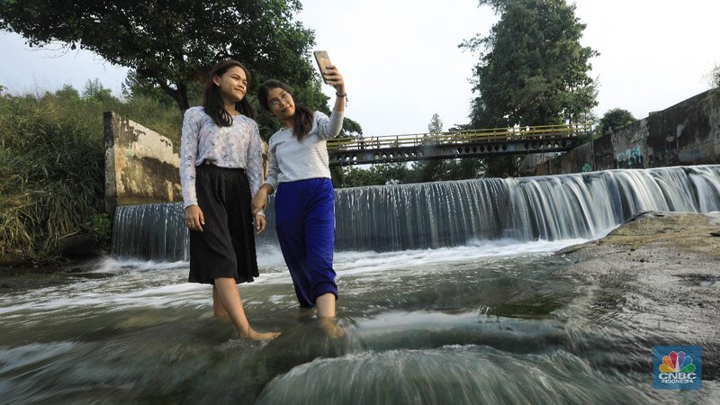 Warga berfoto dengan latar belakang aliran Kali Angke di Situ Lengkong Wetan, Serpong, Tangerang Selatan, Banten, Jumat 12 Juni 2020. Lokasi tersebut menjadi alternatif bagi warga untuk berwisata lokal di tengah masih berlangsungnya penerapan Pembatasan Sosial Berskala Besar (PSBB) di Tangerang Raya untuk menekan penyebaran coronavirus (Covid-19)  (CNBC Indonesia/ Andrean Kristianto)
