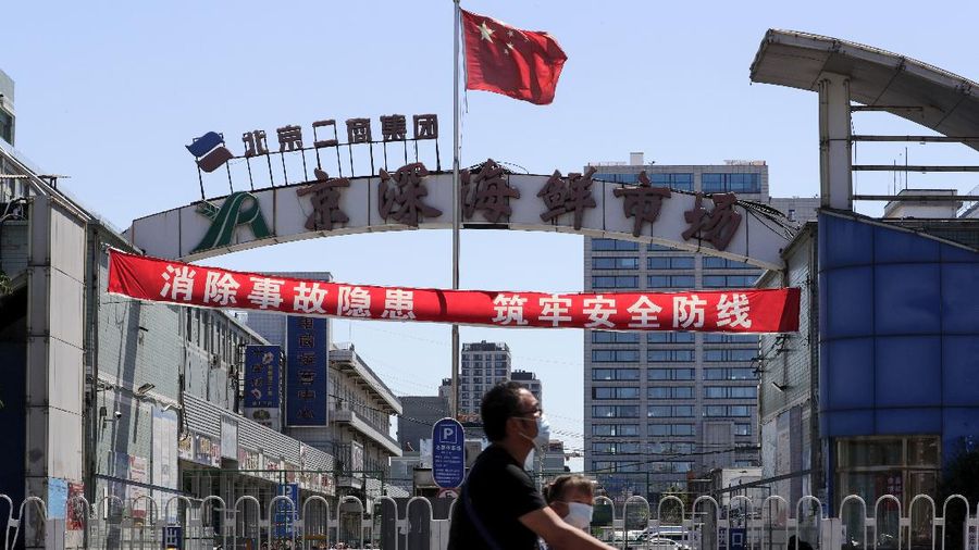 A man and a child wearing protective face masks to help curb the spread of the new coronavirus ride on an electric-powered scooter passes by the seafood wholesale market which was closed for inspection in Beijing, Sunday, June 14, 2020. China is reporting its highest daily total of coronavirus cases in two months after the capital's biggest wholesale food market was shut down following a resurgence in local infections. (AP Photo/Andy Wong)