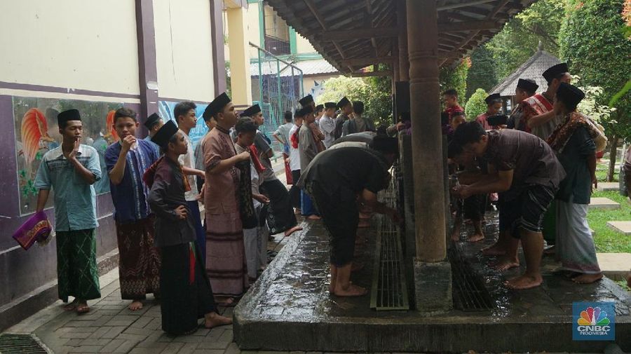 Suasana Pesantren An-Nuqthah, Tangerang Banten, sejumlah santri kembali berdatangan usai belajar di rumah selama pandemi corona. 18/6/20. CNBC Indonesia/Tri Susilo Para santri juga harus mengenakan masker walaupun sudah berada di dalam pesantren. Pemulangan santri ke pesantren dilakukan selama beberapa tahap dalam satu minggu. Ini dilakukan guna menghindari penumpukan orang dalam satu waktu. Pada tahap awal, santri yang kembali baru sekira 15 persen dari total 1.500 santri. Sementara, sebagian orangtua masih khawatir akan penularan virus corona di dalam pesantren. Karena itu mereka membekali buah hatinya dengan cairan pembersih tangan, vitamin dan persediaan masker. Sementara pengelola pesantren menyebut, kebijakan membuka kembali aktifitas belajar tatap muka karena pihaknya merasa sudah sanggup menerapkan protokol kesehatan di dalam pesantren. Guna penerapan protokol kesehatan, pihak pengelola melakukan sterilisasi lingkungan pesantren secara rutin, menata ulang kamar-kamar tidur para santri, dan menjaga jarak antar individu, baik dalam setiap kegiatan belajar mengajar maupun ibadah. Pantauan CNBC Indonesia Dilapangan para santri yang melakukan ibadah harus tetap jaga jarak didalam masjid. Santri yang balik ke pesantren belum semuanya berdatangan, kemungkinan gelombang kedua akan datang pada bulan Juli 2020 mendatang. (CNBC Indonesia/ Tri Susilo)