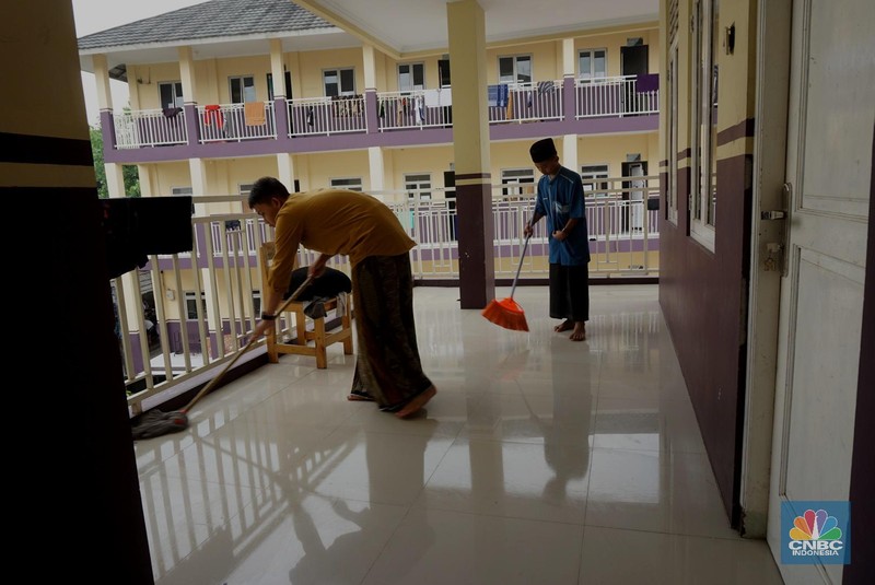 Suasana Pesantren An-Nuqthah, Tangerang Banten, sejumlah santri kembali berdatangan usai belajar di rumah selama pandemi corona. 18/6/20. CNBC Indonesia/Tri Susilo Para santri juga harus mengenakan masker walaupun sudah berada di dalam pesantren. Pemulangan santri ke pesantren dilakukan selama beberapa tahap dalam satu minggu. Ini dilakukan guna menghindari penumpukan orang dalam satu waktu. Pada tahap awal, santri yang kembali baru sekira 15 persen dari total 1.500 santri. Sementara, sebagian orangtua masih khawatir akan penularan virus corona di dalam pesantren. Karena itu mereka membekali buah hatinya dengan cairan pembersih tangan, vitamin dan persediaan masker. Sementara pengelola pesantren menyebut, kebijakan membuka kembali aktifitas belajar tatap muka karena pihaknya merasa sudah sanggup menerapkan protokol kesehatan di dalam pesantren. Guna penerapan protokol kesehatan, pihak pengelola melakukan sterilisasi lingkungan pesantren secara rutin, menata ulang kamar-kamar tidur para santri, dan menjaga jarak antar individu, baik dalam setiap kegiatan belajar mengajar maupun ibadah. Pantauan CNBC Indonesia Dilapangan para santri yang melakukan ibadah harus tetap jaga jarak didalam masjid. Santri yang balik ke pesantren belum semuanya berdatangan, kemungkinan gelombang kedua akan datang pada bulan Juli 2020 mendatang. (CNBC Indonesia/ Tri Susilo)