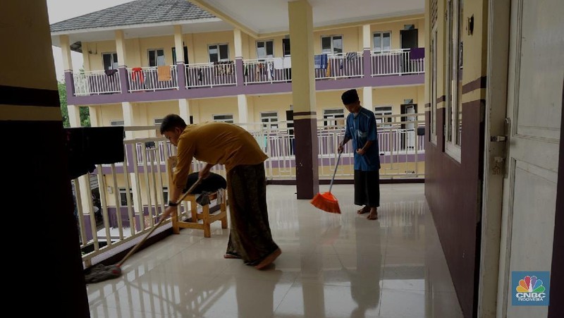 Suasana Pesantren An-Nuqthah, Tangerang Banten, sejumlah santri kembali berdatangan usai belajar di rumah selama pandemi corona. 18/6/20. CNBC Indonesia/Tri Susilo Para santri juga harus mengenakan masker walaupun sudah berada di dalam pesantren. Pemulangan santri ke pesantren dilakukan selama beberapa tahap dalam satu minggu. Ini dilakukan guna menghindari penumpukan orang dalam satu waktu. Pada tahap awal, santri yang kembali baru sekira 15 persen dari total 1.500 santri. Sementara, sebagian orangtua masih khawatir akan penularan virus corona di dalam pesantren. Karena itu mereka membekali buah hatinya dengan cairan pembersih tangan, vitamin dan persediaan masker. Sementara pengelola pesantren menyebut, kebijakan membuka kembali aktifitas belajar tatap muka karena pihaknya merasa sudah sanggup menerapkan protokol kesehatan di dalam pesantren. Guna penerapan protokol kesehatan, pihak pengelola melakukan sterilisasi lingkungan pesantren secara rutin, menata ulang kamar-kamar tidur para santri, dan menjaga jarak antar individu, baik dalam setiap kegiatan belajar mengajar maupun ibadah. Pantauan CNBC Indonesia Dilapangan para santri yang melakukan ibadah harus tetap jaga jarak didalam masjid. Santri yang balik ke pesantren belum semuanya berdatangan, kemungkinan gelombang kedua akan datang pada bulan Juli 2020 mendatang. (CNBC Indonesia/ Tri Susilo)