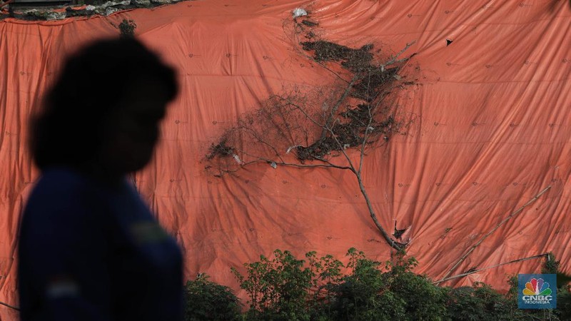 Warga bersantai di sekitar Banjir Kanal Timur di depan lokasi tanah longsor yang ditutupi terpal besar di pinggir Kanal Banjir Timur, Jakarta, Kamis (18/6/2020). Longsor yang terjadi pada awal Januari 2020 tersebut belum diperbaiki dan hanya ditutupi terpal besar guna mengantisipasi longsor susulan. Warga setempat mengaku khawatir terjadi longsor susulan karena terpal dan karung pasir yang digunakan untuk menutupi lokasi longsor kian rapuh. Pantauan CNBC Indonesia disekitar lokasi banyak aktivitas yang bermain dan berkumpul. Seperti diketahui longsor tersebut terjadi akibat hujan deras saat awal tahun lalu. Penutupan itu guna mencegah longsor susulan.  (CNBC Indonesia/ Muhammad Sabki)