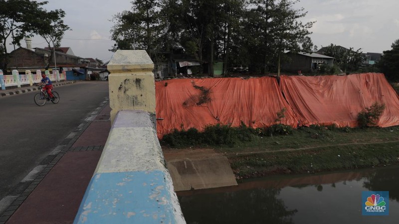 Warga bersantai di sekitar Banjir Kanal Timur di depan lokasi tanah longsor yang ditutupi terpal besar di pinggir Kanal Banjir Timur, Jakarta, Kamis (18/6/2020). Longsor yang terjadi pada awal Januari 2020 tersebut belum diperbaiki dan hanya ditutupi terpal besar guna mengantisipasi longsor susulan. Warga setempat mengaku khawatir terjadi longsor susulan karena terpal dan karung pasir yang digunakan untuk menutupi lokasi longsor kian rapuh. Pantauan CNBC Indonesia disekitar lokasi banyak aktivitas yang bermain dan berkumpul. Seperti diketahui longsor tersebut terjadi akibat hujan deras saat awal tahun lalu. Penutupan itu guna mencegah longsor susulan.  (CNBC Indonesia/ Muhammad Sabki)