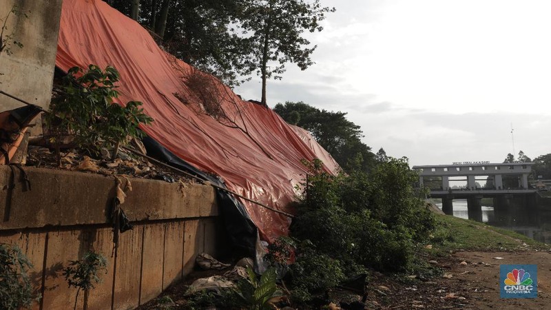 Warga bersantai di sekitar Banjir Kanal Timur di depan lokasi tanah longsor yang ditutupi terpal besar di pinggir Kanal Banjir Timur, Jakarta, Kamis (18/6/2020). Longsor yang terjadi pada awal Januari 2020 tersebut belum diperbaiki dan hanya ditutupi terpal besar guna mengantisipasi longsor susulan. Warga setempat mengaku khawatir terjadi longsor susulan karena terpal dan karung pasir yang digunakan untuk menutupi lokasi longsor kian rapuh. Pantauan CNBC Indonesia disekitar lokasi banyak aktivitas yang bermain dan berkumpul. Seperti diketahui longsor tersebut terjadi akibat hujan deras saat awal tahun lalu. Penutupan itu guna mencegah longsor susulan.  (CNBC Indonesia/ Muhammad Sabki)
