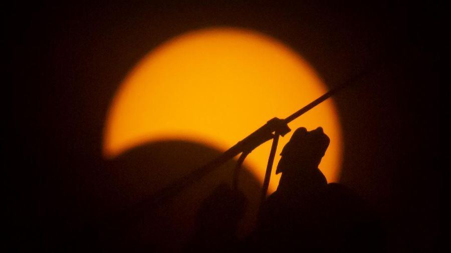A figure on a roof eave of the historic Bell Tower is silhouetted by the sun during a partial solar eclipse in Beijing, Sunday, June 21, 2020. (AP Photo/Mark Schiefelbein)