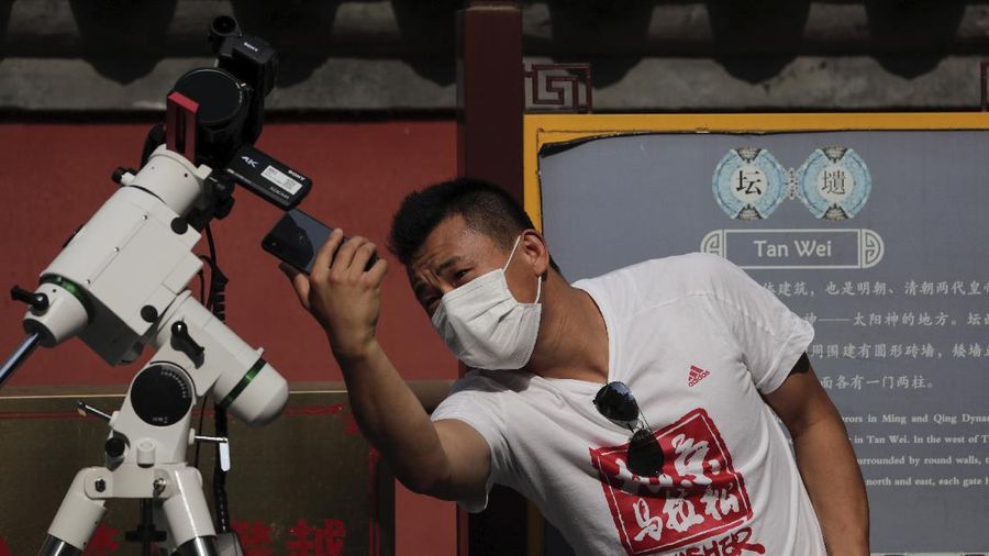 A man tries to take photos as a solar eclipse is seen over the sky in Chiayi City, southwest of Taiwan, Sunday, June 21, 2020. (AP Photo/Chiang Ying-ying)
