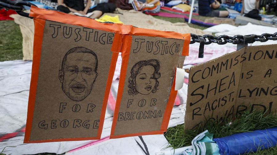 Protesters rest in a grassy area surrounded by signs calling for changes to police policies and practices at an encampment outside City Hall, Friday, June 26, 2020, in New York. (AP Photo/John Minchillo)