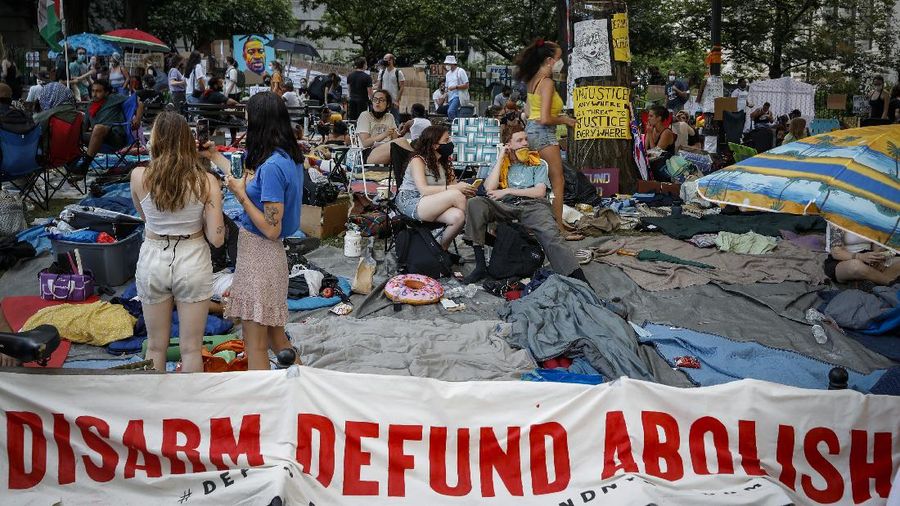 Protesters rest in a grassy area surrounded by signs calling for changes to police policies and practices at an encampment outside City Hall, Friday, June 26, 2020, in New York. (AP Photo/John Minchillo)