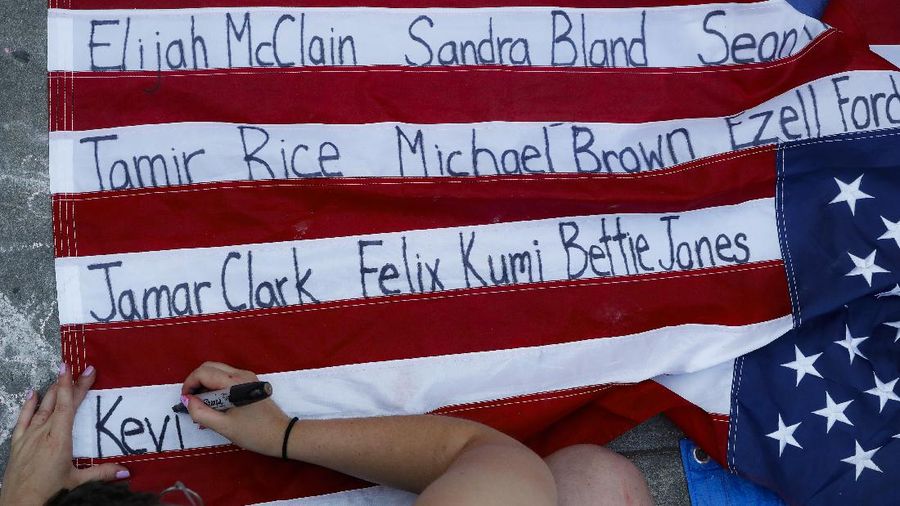 Protesters rest in a grassy area surrounded by signs calling for changes to police policies and practices at an encampment outside City Hall, Friday, June 26, 2020, in New York. (AP Photo/John Minchillo)