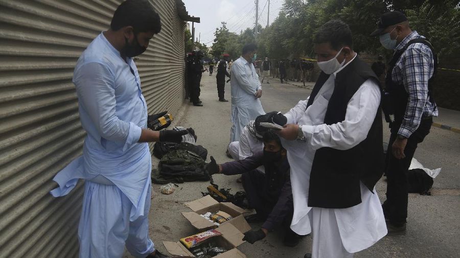 In this image made from a video, police and investigators gather around a car used by attackers, in Karachi, Pakistan Monday, June 29, 2020. Militants attacked the stock exchange in the Pakistani city of Karachi on Monday, according to police. (AP Photo)