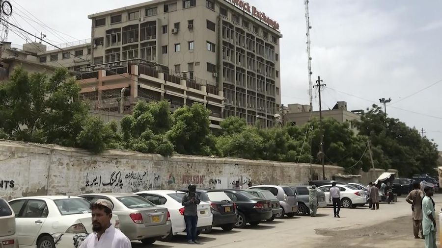 In this image made from a video, police and investigators gather around a car used by attackers, in Karachi, Pakistan Monday, June 29, 2020. Militants attacked the stock exchange in the Pakistani city of Karachi on Monday, according to police. (AP Photo)