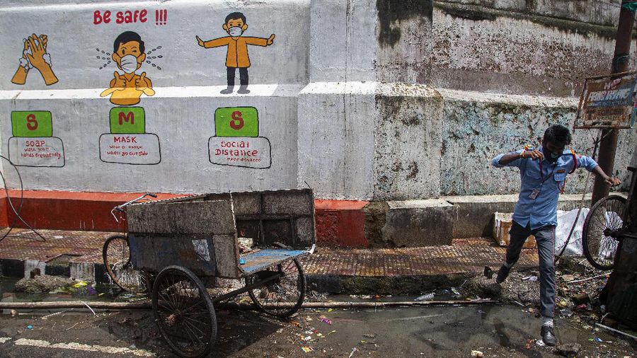 An Indian security guard jumps to cross a puddle of water next to a wall painted with murals informing people about precautions against the coronavirus during the reimposed lockdown in Gauhati, India, Monday, June 29, 2020. India has reported a new daily record of nearly 20,000 new infections as several Indian states reimpose partial or full lockdowns to stem the spread of the coronavirus. (AP Photo/Anupam Nath)