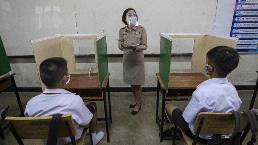 Teachers and students wearing protective gear to help curb the spread of the coronavirus as they pray before class at Samkhok School in Pathum Thani, outside Bangkok, Wednesday, July 1, 2020. Thailand has begun a fifth phase of relaxations of COVID-19 restrictions, allowing the reopening of schools and high-risk entertainment venues such as pubs and massage parlors that had been shut since mid-March. (AP Photo/Sakchai Lalit)