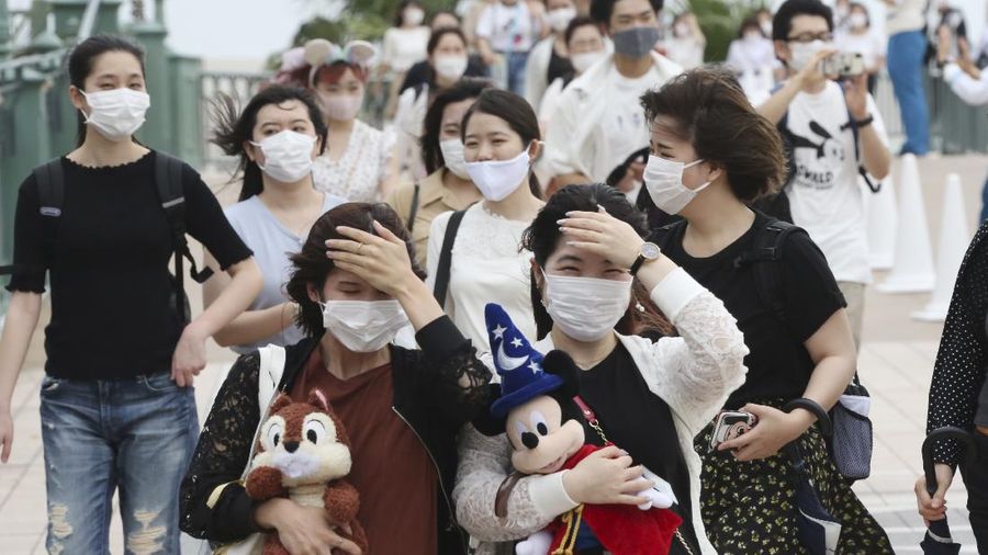 A visitor gestures to have the body temperature of a Mickey Mouse doll checked at the entrance of Tokyo Disneyland in Urayasu, near Tokyo, Wednesday, July 1, 2020. Tokyo Disneyland reopened for the first time in four months after suspending operations due to coronavirus concerns. (Kyodo News via AP)