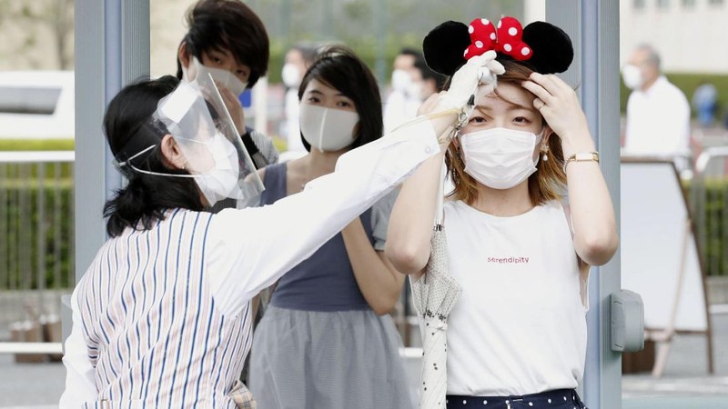 A visitor gestures to have the body temperature of a Mickey Mouse doll checked at the entrance of Tokyo Disneyland in Urayasu, near Tokyo, Wednesday, July 1, 2020. Tokyo Disneyland reopened for the first time in four months after suspending operations due to coronavirus concerns. (Kyodo News via AP)