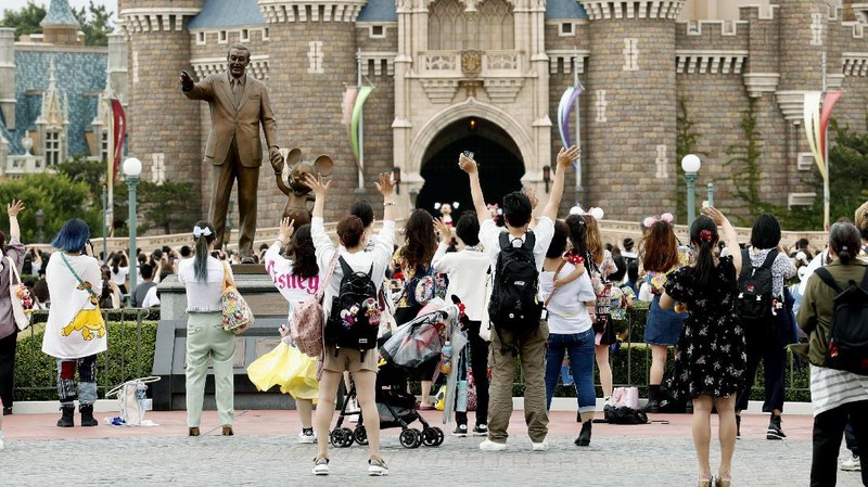 A visitor gestures to have the body temperature of a Mickey Mouse doll checked at the entrance of Tokyo Disneyland in Urayasu, near Tokyo, Wednesday, July 1, 2020. Tokyo Disneyland reopened for the first time in four months after suspending operations due to coronavirus concerns. (Kyodo News via AP)