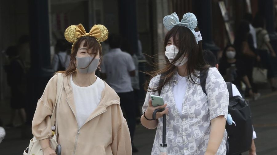 A visitor gestures to have the body temperature of a Mickey Mouse doll checked at the entrance of Tokyo Disneyland in Urayasu, near Tokyo, Wednesday, July 1, 2020. Tokyo Disneyland reopened for the first time in four months after suspending operations due to coronavirus concerns. (Kyodo News via AP)