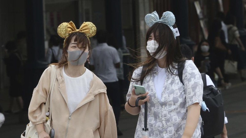 A visitor gestures to have the body temperature of a Mickey Mouse doll checked at the entrance of Tokyo Disneyland in Urayasu, near Tokyo, Wednesday, July 1, 2020. Tokyo Disneyland reopened for the first time in four months after suspending operations due to coronavirus concerns. (Kyodo News via AP)