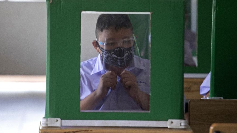 Teachers and students wearing protective gear to help curb the spread of the coronavirus as they pray before class at Samkhok School in Pathum Thani, outside Bangkok, Wednesday, July 1, 2020. Thailand has begun a fifth phase of relaxations of COVID-19 restrictions, allowing the reopening of schools and high-risk entertainment venues such as pubs and massage parlors that had been shut since mid-March. (AP Photo/Sakchai Lalit)