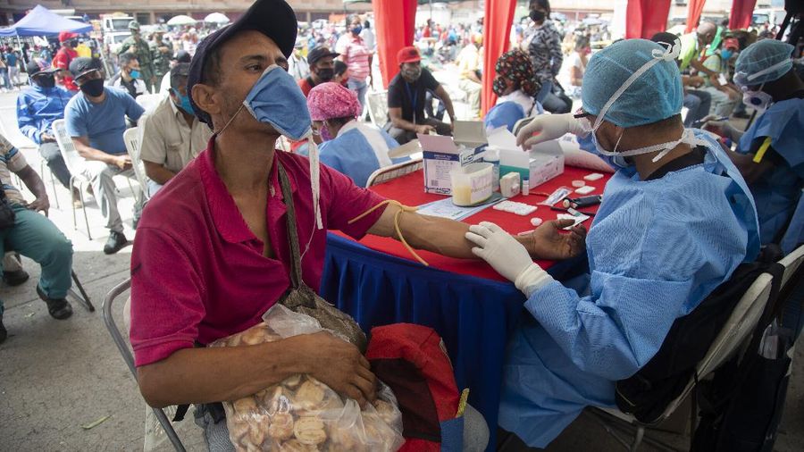 A health worker takes a blood sample for a quick COVID-19 test from man who works selling cookies at the Coche food market in Caracas, Venezuela, Tuesday, June 23, 2020. Health authorities tested people arriving at the market as a preventive measure to help curb the spread of the new coronavirus. (AP Photo/Ariana Cubillos)