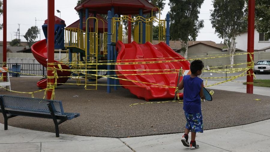 A boy walks with his skateboard past a playground sealed off due to the coronavirus pandemic, Wednesday, July 1, 2020, in Commerce, Calif. California Gov. Gavin Newsom has ordered a three-week closure of bars and indoor operations of restaurants certain other businesses in Los Angeles and 18 other counties. (AP Photo/Jae C. Hong)