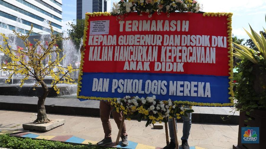 Warga melintas di depan karangan bunga sebagai protes terhadap PPDB DKI, berjejer di Balai Kota DKI Jakarta, Senin (6/7).Karangan bunga berisi pesan kekecewaan dari para orang tua murid berjejer di depan pintu masuk Balai Kota DKI Jakarta. Mereka kecewa dengan aturan penerimaan peserta didik baru (PPDB) DKI Jakarta. (CNBC Indonesia/ Muhammad Sabki)