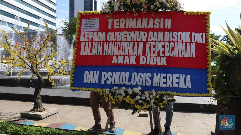 Warga melintas di depan karangan bunga sebagai protes terhadap PPDB DKI, berjejer di Balai Kota DKI Jakarta, Senin (6/7).Karangan bunga berisi pesan kekecewaan dari para orang tua murid berjejer di depan pintu masuk Balai Kota DKI Jakarta. Mereka kecewa dengan aturan penerimaan peserta didik baru (PPDB) DKI Jakarta. (CNBC Indonesia/ Muhammad Sabki)