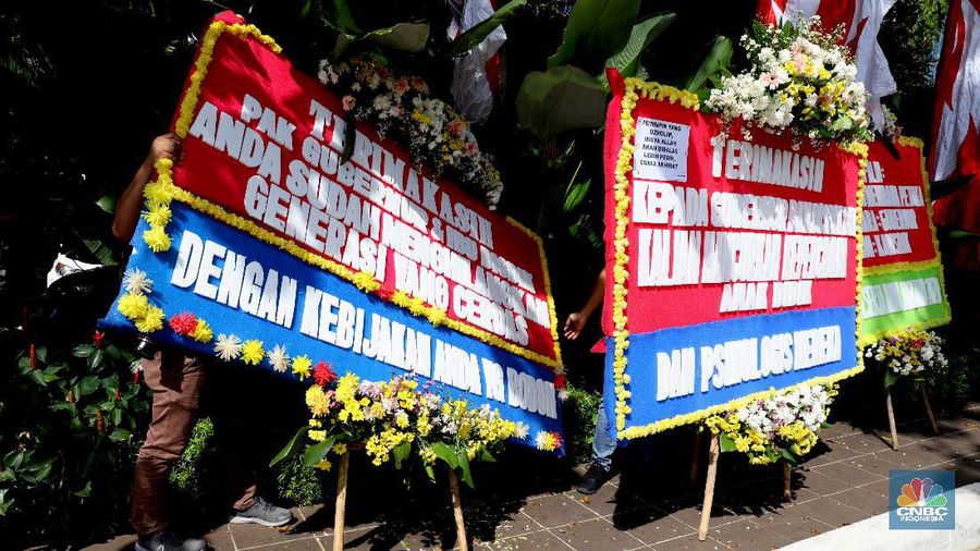 Warga melintas di depan karangan bunga sebagai protes terhadap PPDB DKI, berjejer di Balai Kota DKI Jakarta, Senin (6/7).Karangan bunga berisi pesan kekecewaan dari para orang tua murid berjejer di depan pintu masuk Balai Kota DKI Jakarta. Mereka kecewa dengan aturan penerimaan peserta didik baru (PPDB) DKI Jakarta. (CNBC Indonesia/ Muhammad Sabki)