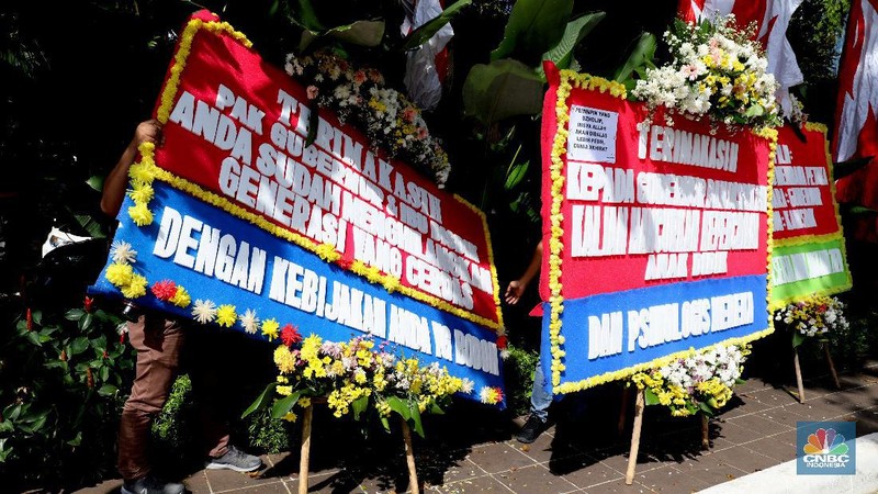 Warga melintas di depan karangan bunga sebagai protes terhadap PPDB DKI, berjejer di Balai Kota DKI Jakarta, Senin (6/7).Karangan bunga berisi pesan kekecewaan dari para orang tua murid berjejer di depan pintu masuk Balai Kota DKI Jakarta. Mereka kecewa dengan aturan penerimaan peserta didik baru (PPDB) DKI Jakarta. (CNBC Indonesia/ Muhammad Sabki)