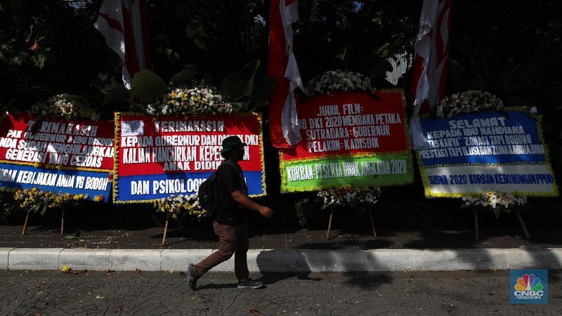 Warga melintas di depan karangan bunga sebagai protes terhadap PPDB DKI, berjejer di Balai Kota DKI Jakarta, Senin (6/7).Karangan bunga berisi pesan kekecewaan dari para orang tua murid berjejer di depan pintu masuk Balai Kota DKI Jakarta. Mereka kecewa dengan aturan penerimaan peserta didik baru (PPDB) DKI Jakarta. (CNBC Indonesia/ Muhammad Sabki)