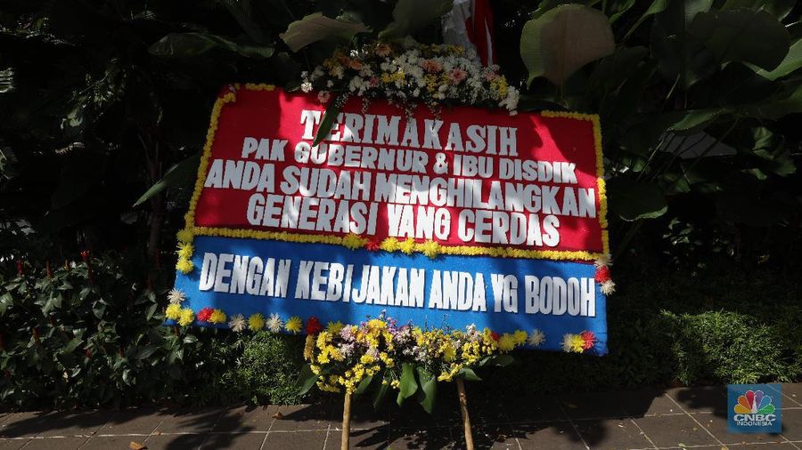Warga melintas di depan karangan bunga sebagai protes terhadap PPDB DKI, berjejer di Balai Kota DKI Jakarta, Senin (6/7).Karangan bunga berisi pesan kekecewaan dari para orang tua murid berjejer di depan pintu masuk Balai Kota DKI Jakarta. Mereka kecewa dengan aturan penerimaan peserta didik baru (PPDB) DKI Jakarta. (CNBC Indonesia/ Muhammad Sabki)