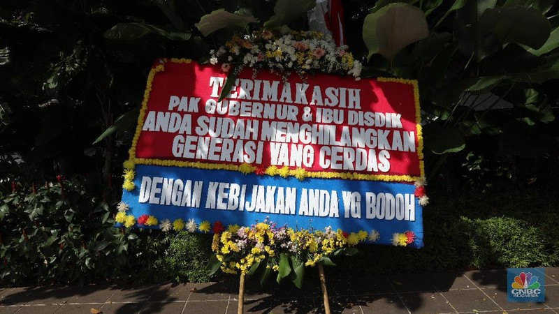 Warga melintas di depan karangan bunga sebagai protes terhadap PPDB DKI, berjejer di Balai Kota DKI Jakarta, Senin (6/7).Karangan bunga berisi pesan kekecewaan dari para orang tua murid berjejer di depan pintu masuk Balai Kota DKI Jakarta. Mereka kecewa dengan aturan penerimaan peserta didik baru (PPDB) DKI Jakarta. (CNBC Indonesia/ Muhammad Sabki)