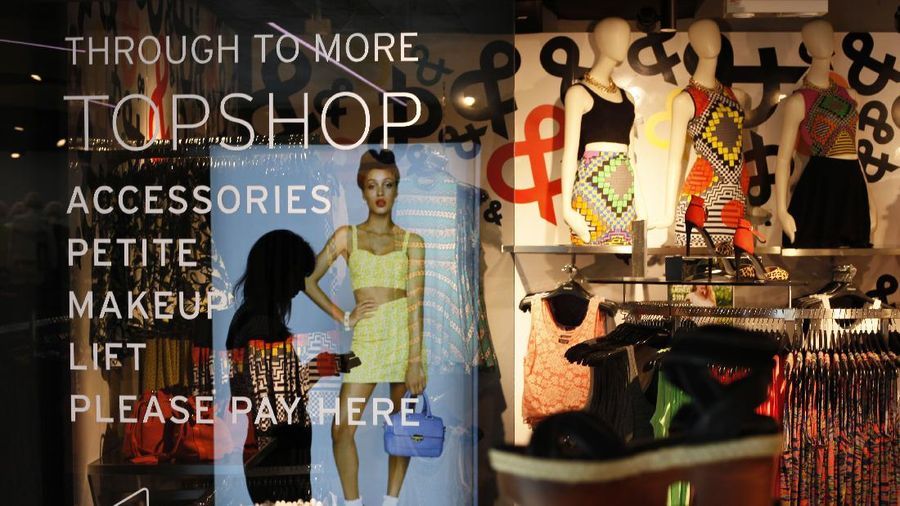 A woman playing with a smartphone is reflected on a window glass at a new Topshop store in central Hong Kong Wednesday June 5, 2013. The British fashion brand is launching it first store in Hong Kong which will be open to the public on Thursday. (AP Photo/Kin Cheung)
