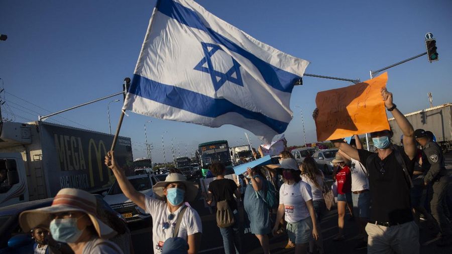 Israeli social workers wave a national flag as they block a main road during a protest against the economic situation in the central Israeli town of Kfar Ahim, Thursday, July 9, 2020. With a new outbreak of coronavirus devastating Israel's economy, one of Prime Minister Benjamin Netanyahu's closest confidants was dispatched on to a TV studio on a recent day to calm the nerves of a jittery nation. Instead, he dismissed the public's economic pain as 