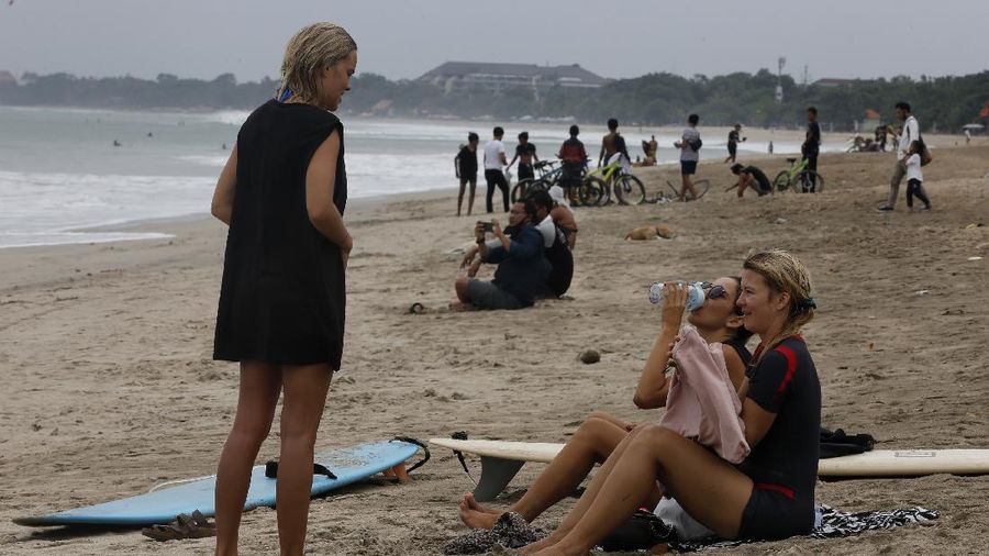 Tourists wearing face masks carry their surfboard at Kuta beach, Bali, Indonesia on Thursday, July 9, 2020. Indonesia's resort island of Bali reopened after a three-month virus lockdown Thursday, allowing local people and stranded foreign tourists to resume public activities before foreign arrivals resume in September.(AP Photo/Firdia Lisnawati)