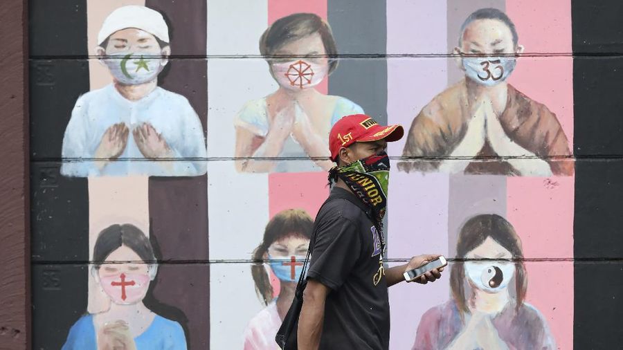 A man wearing a face mask walks past a coronavirus awareness mural depicting children of various faiths praying while wearing face masks in Depok, Indonesia, Wednesday, July 8, 2020. (AP Photo/Dita Alangkara)