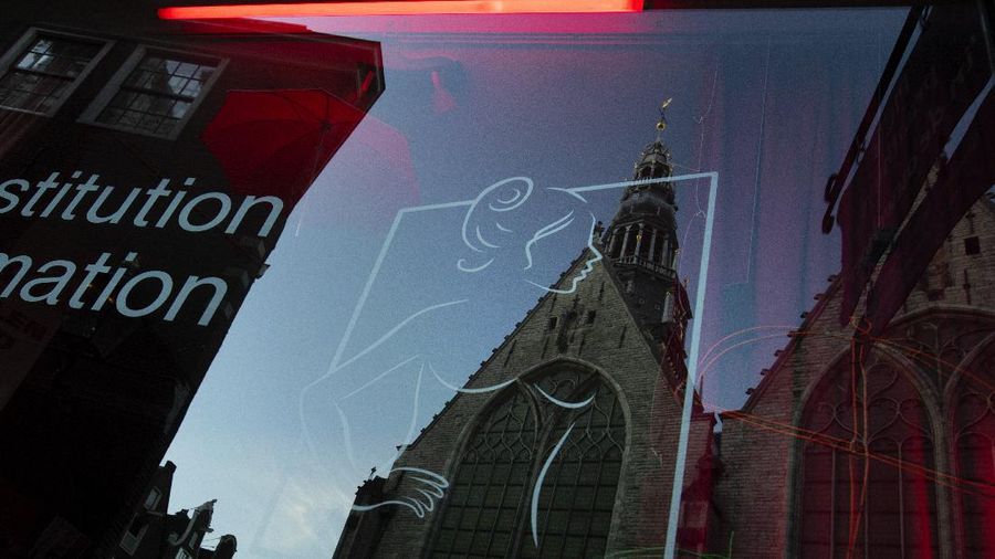 Oude Kerk, or Old Church, is reflected in the window of the PIC, Prostitution Information Center, as sex workers welcomed clients again in the Red Light District in Amsterdam, Netherlands, Wednesday, July 1, 2020. It wasn't quite business as usual as the capital's Red Light District emerged from coronavirus lockdown, but it was as close as it has been since the pandemic slammed the brakes on the world's oldest profession. (AP Photo/Peter Dejong)