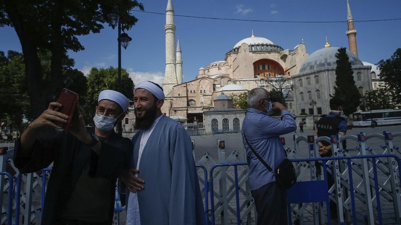People use their mobile to take a selfie picture outside the now closed Byzantine-era Hagia Sophia, one of Istanbul's main tourist attractions in the historic Sultanahmet district of Istanbul, Saturday, July 11, 2020. Turkey's President Recep Tayyip Erdogan formally reconverted Hagia Sophia into a mosque and declared it open for Muslim worship, hours after a high court annulled a 1934 decision that had made the religious landmark a museum.The decision sparked deep dismay among Orthodox Christians. Originally a cathedral, Hagia Sophia was turned into a mosque after Istanbul's conquest by the Ottoman Empire but had been a museum for the last 86 years, drawing millions of tourists annually. (AP Photo/Emrah Gurel)