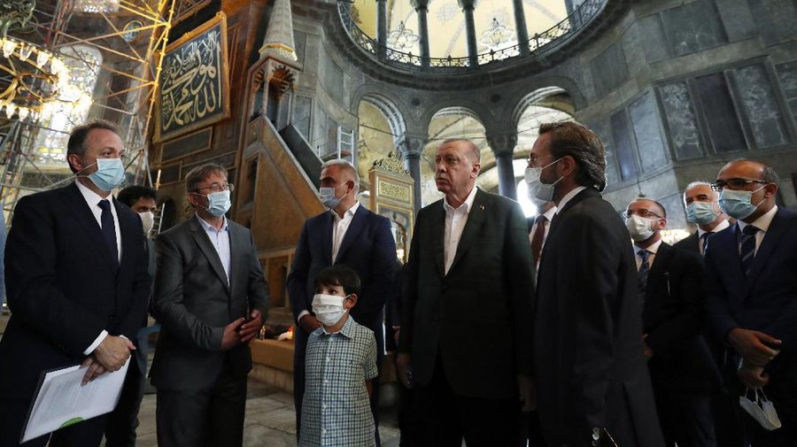 Turkey's President Recep Tayyip Erdogan, center, salutes supporters as he visits the Byzantine-era Hagia Sophia, in the background, one of Istanbul's main tourist attractions in the historic Sultanahmet district of Istanbul, Sunday, July 19, 2020, days after he formally reconverted Hagia Sophia into a mosque and declared it open for Muslim worship, after a high court annulled a 1934 decision that had made the religious landmark a museum.(Turkish Presidency via AP, Pool)